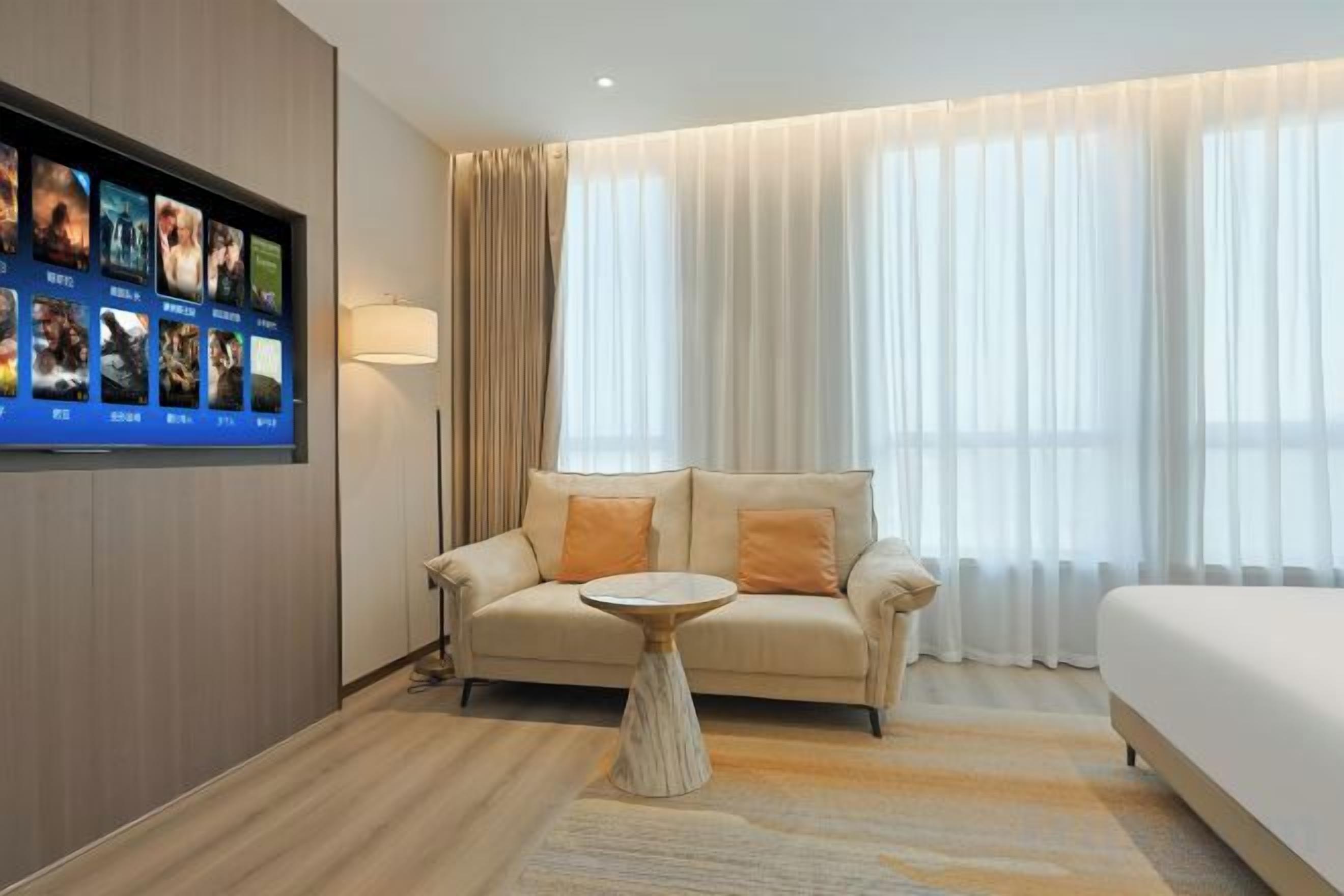 Habitación de hotel con sofá, una mesita redonda, cama y televisor montado en la pared.