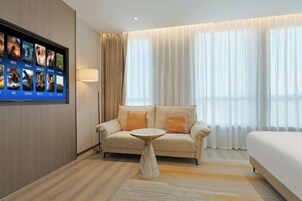 A hotel room with a sofa, a small round table, a bed, and a TV mounted on the wall.