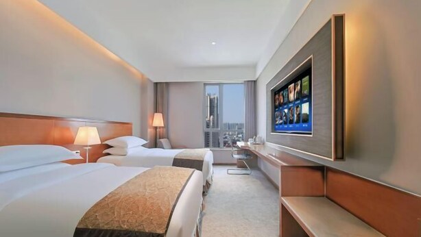 Een hotelkamer met twee bedden, een televisie, een bureau en uitzicht op de stad.