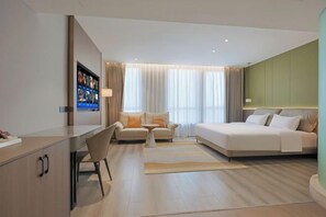 A hotel room with a bed, a desk, a chair, a sofa, and a television.
