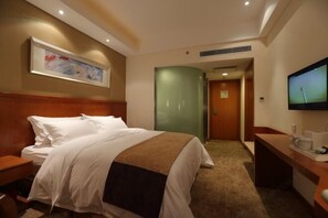 A hotel room with a bed, a desk with a television, and a painting on the wall.