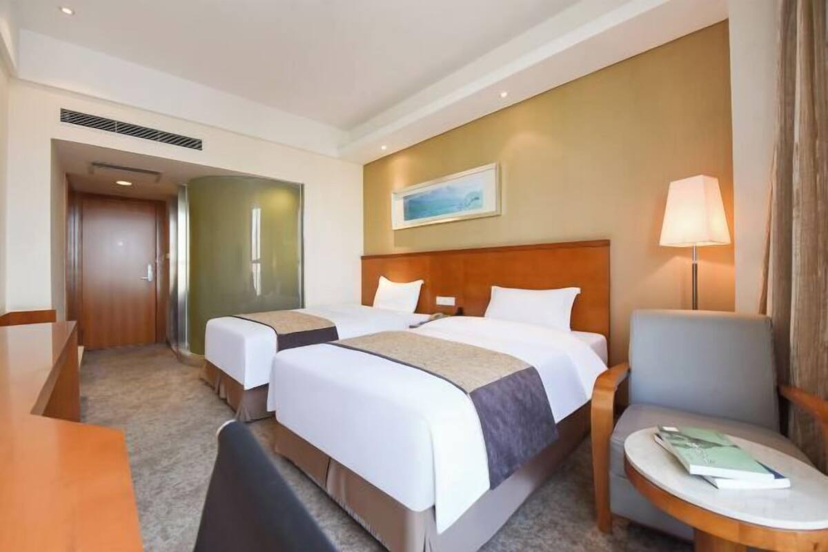 A hotel room with two beds, a desk, a chair, and a small table.