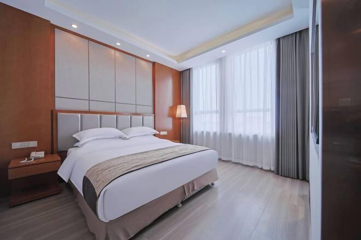 A hotel room with a large bed, a bedside table, a lamp, and a window with curtains.