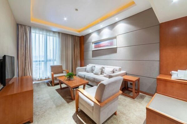 A modern hotel room with a sofa, armchairs, a coffee table, and a TV.