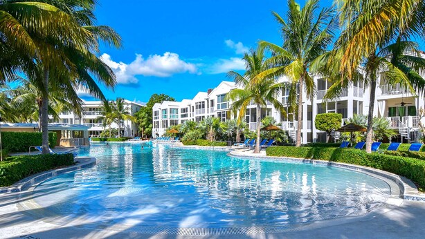 Una piscina rodeada de palmeras y edificios blancos con balcones.