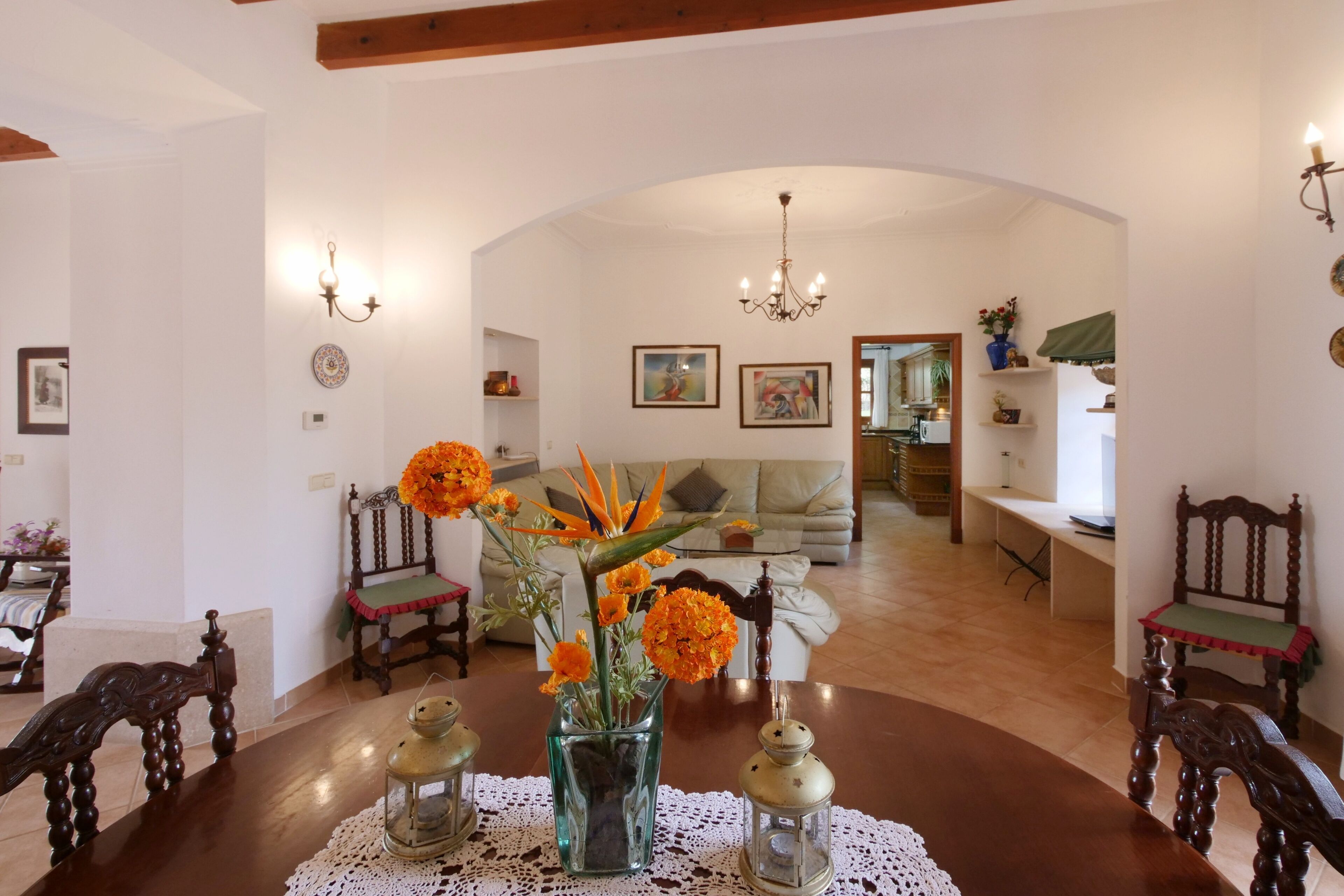 Zona pranzo con tavolo in legno, sedie, un vaso con fiori arancioni e un lampadario.