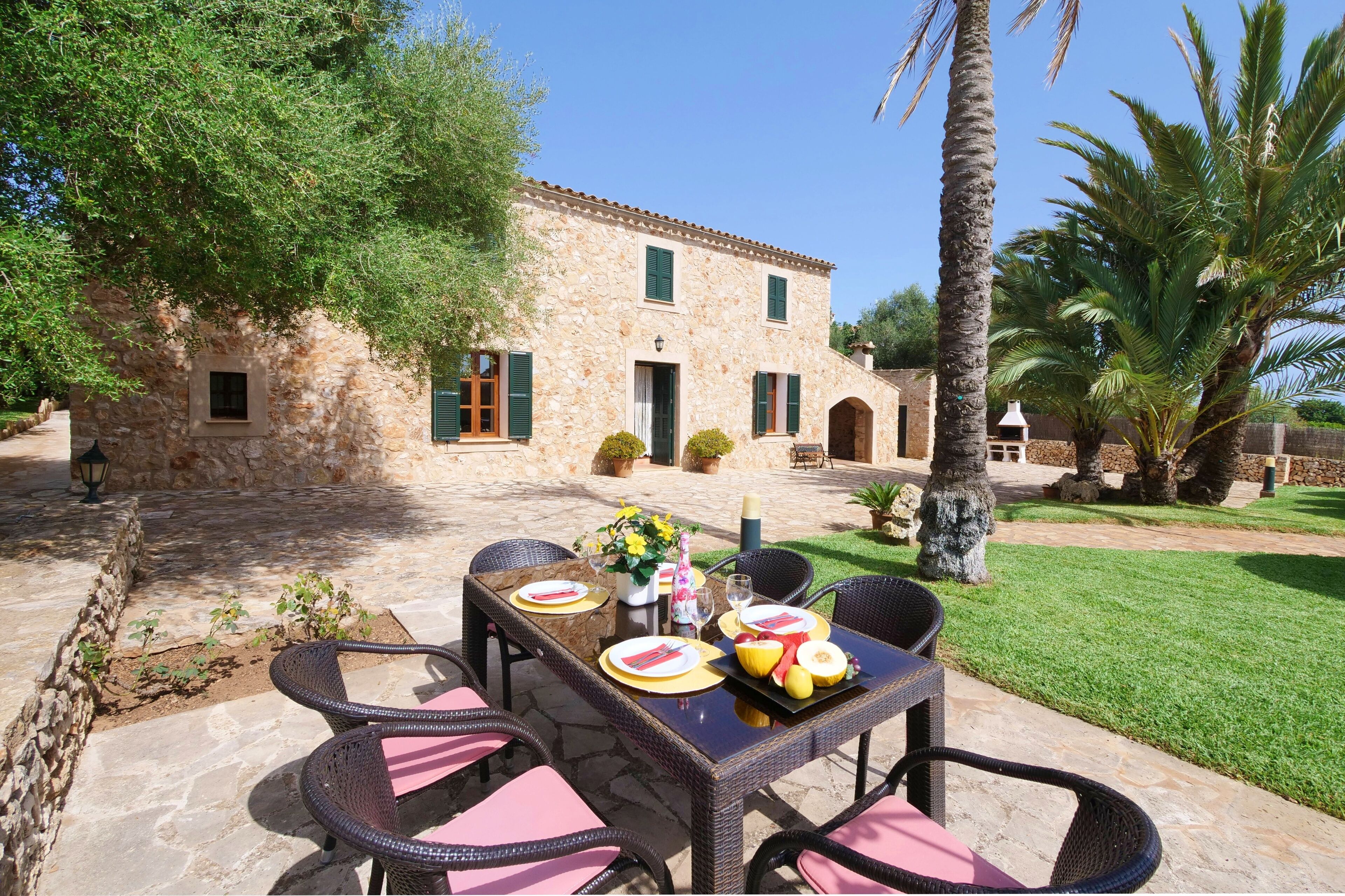 Un edificio in pietra con un tavolo da pranzo in veranda, immerso nel verde e palme.