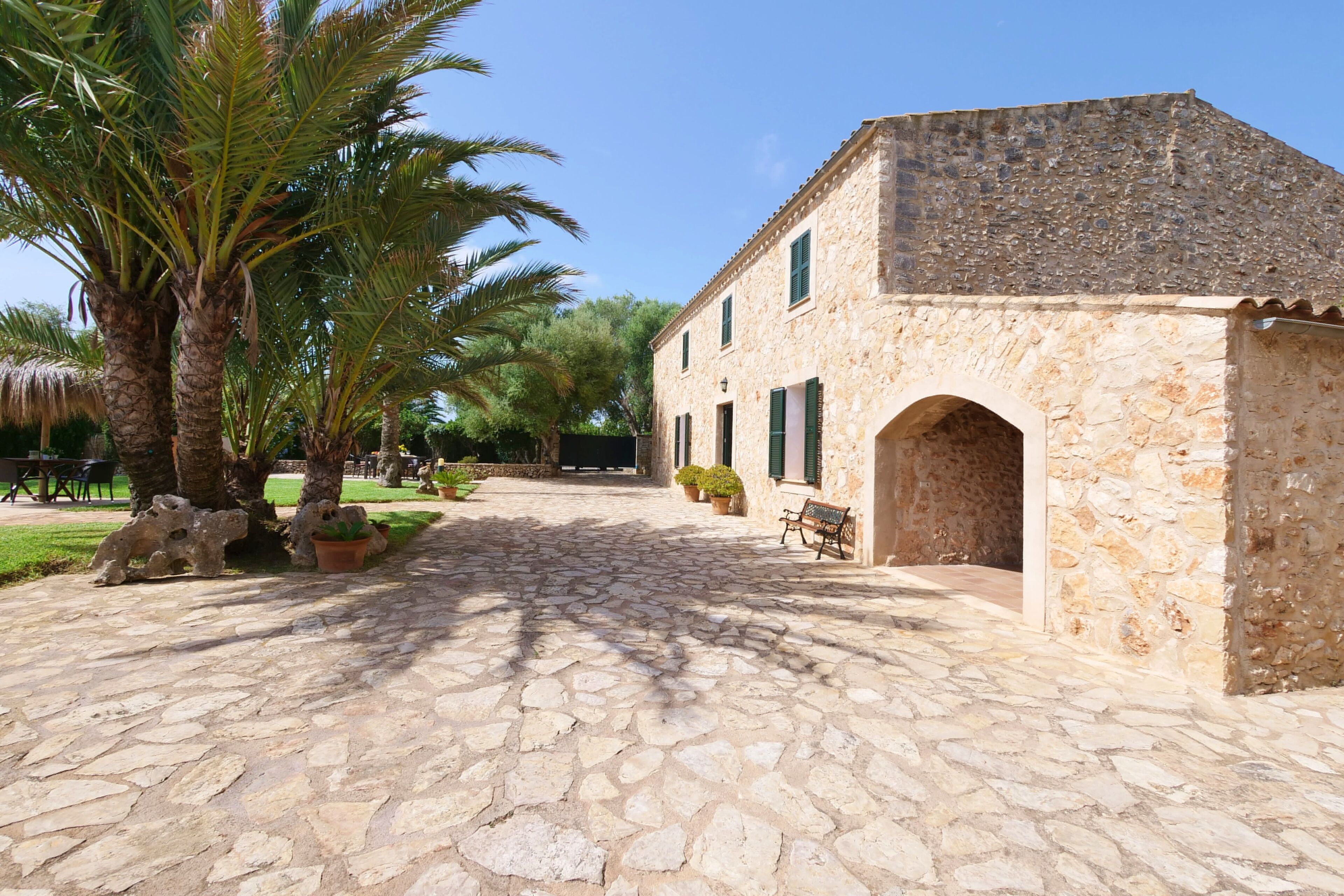 A stone building with a tiled courtyard, palm trees, and a bench.