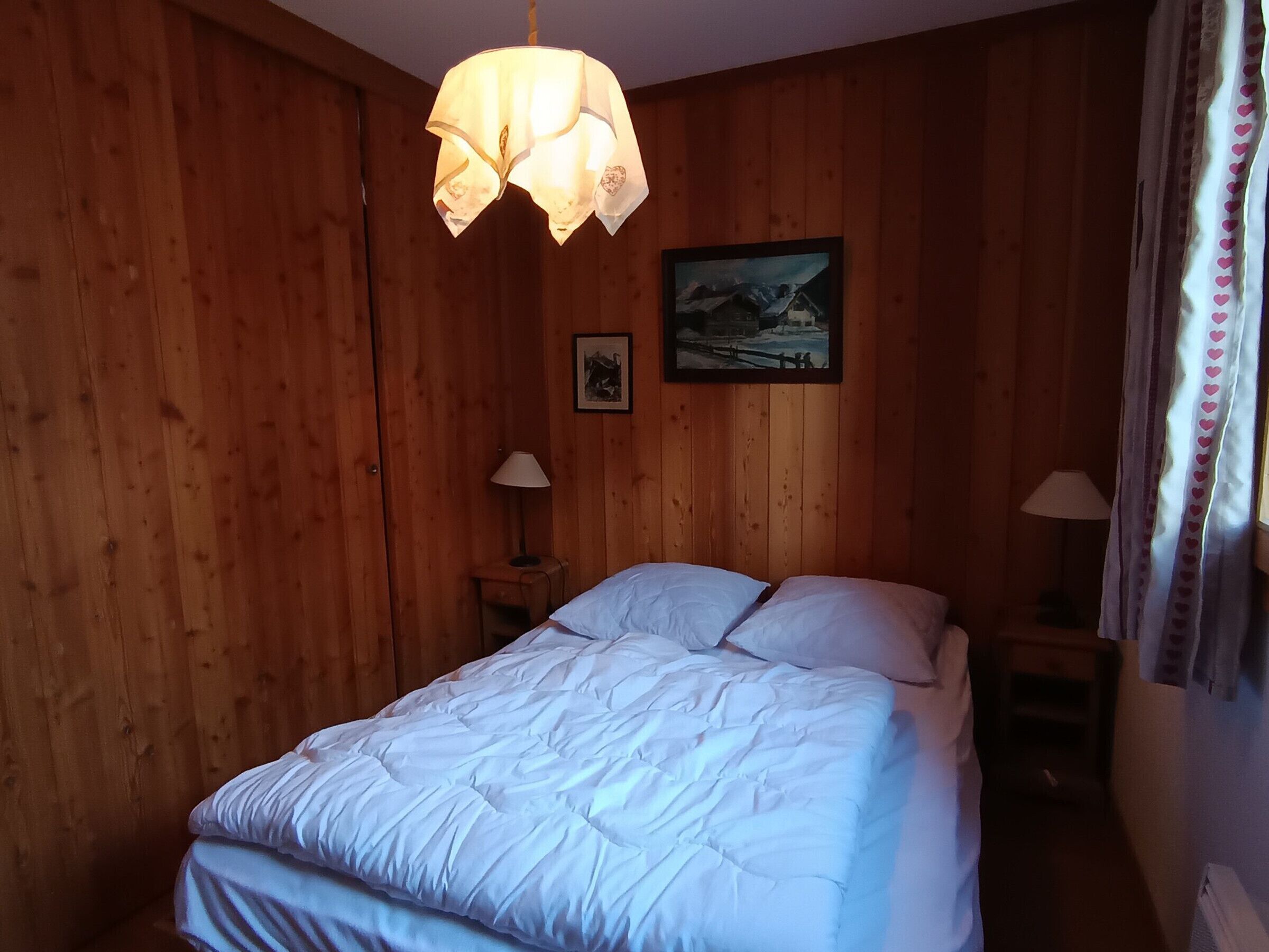 Habitación con paneles de madera, una cama, dos lámparas de noche, un cuadro en la pared y una lámpara colgante.