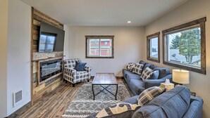 A cozy living room with a fireplace, a sofa, a coffee table, and a TV mounted on a wooden wall. - Newly Built Bigfork Gem ~ 1 Mi to Fish & Hike (Bigfork)