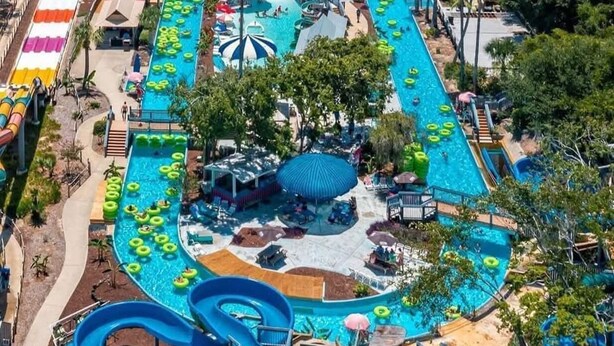 An aerial view of a water park with multiple slides and pools, surrounded by buildings and palm trees. - 🌴Ground Floor Condo~Private Path2Beach~Pool~2BR St. Martin Beachwalk Villas 311 (Destin)