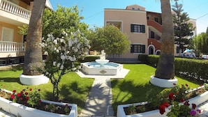 A courtyard with a central fountain, surrounded by palm trees and flower beds. - Eriva Hotel (Acharavi)