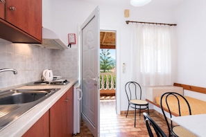 Eine kompakte Küche mit Spüle, Herd und Schränken, die auf einen Balkon mit Tisch und Stühlen führt.