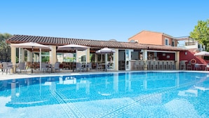 A swimming pool with tiled patterns, outdoor seating with umbrellas, and a building with a tiled roof. - Eriva Hotel (Acharavi)
