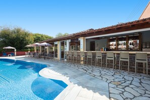 Ein Barbereich am Pool mit Steinböden, Sitzgelegenheiten im Freien und einem klaren, blauen Pool.