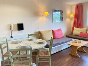 A cozy room with a dining table set for four, a sofa with cushions, a small wooden table, and a wall-mounted telephone. - 2-room apartment, ski-in/ski-out, 5 persons, Avoriaz (Avoriaz)
