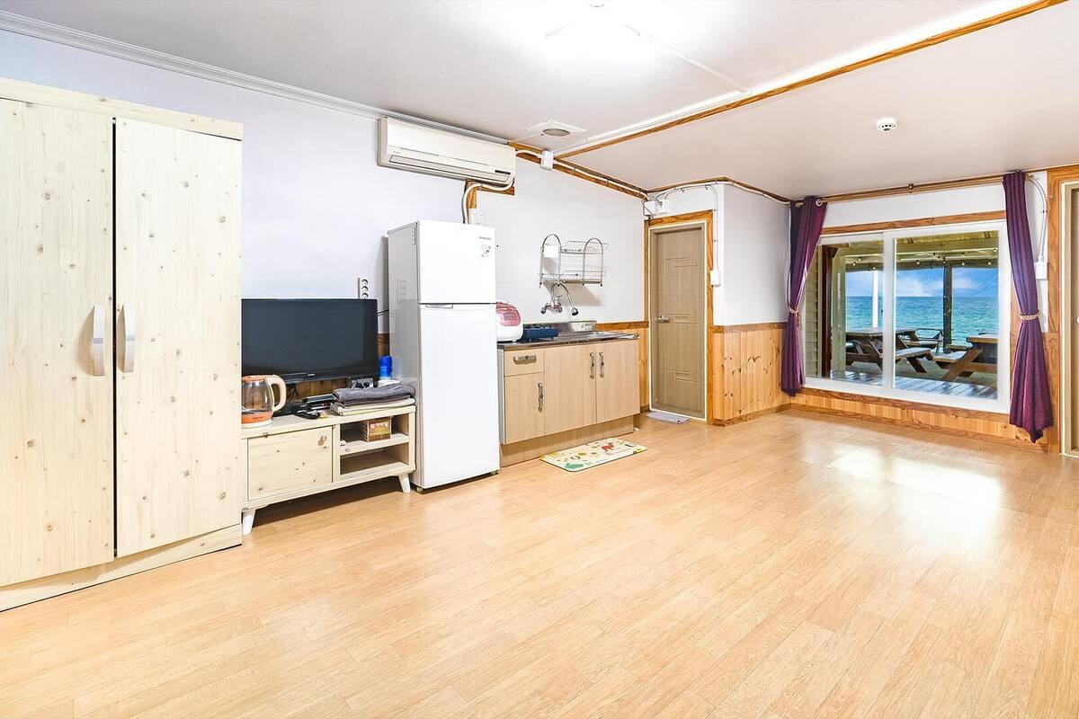 Ein kompakter Raum mit einer Küchenzeile, einem Fernseher und Meerblick durch ein großes Fenster.