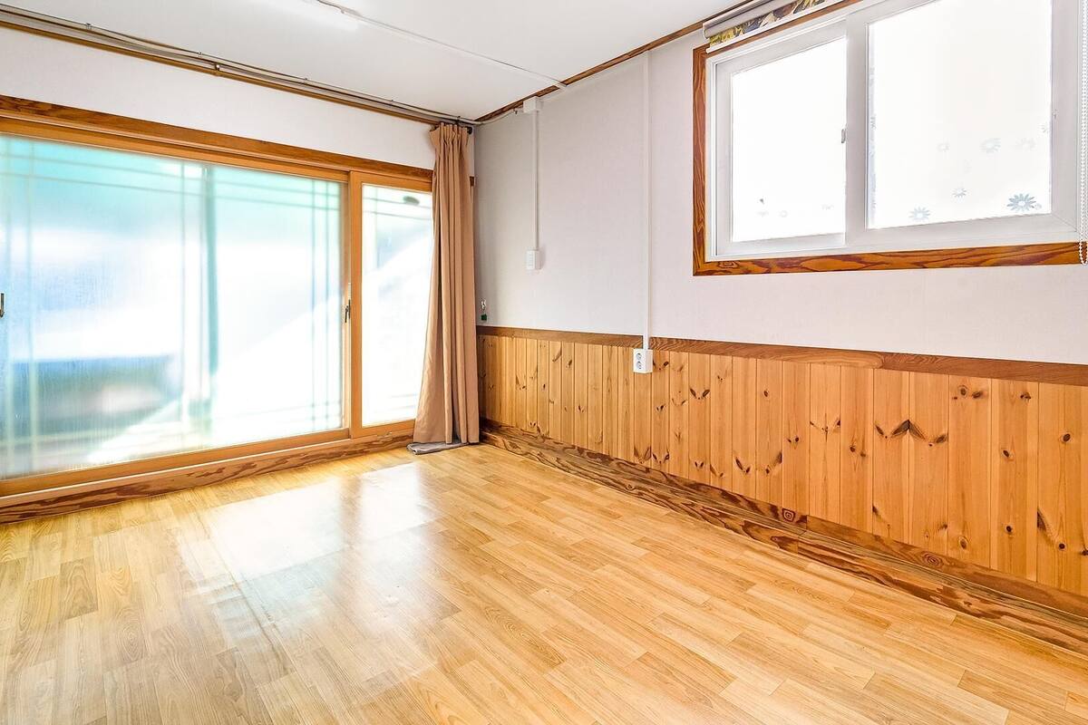 Ein Zimmer mit Holzboden, einer großen Schiebetür aus Glas und einem Fenster mit Holzrahmen.