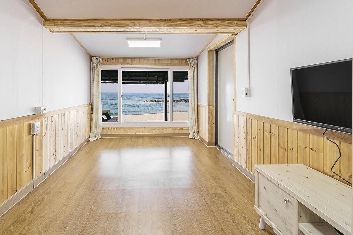 Ein Flur mit Holzwandverkleidung, einem Fernseher und Blick auf den Strand.