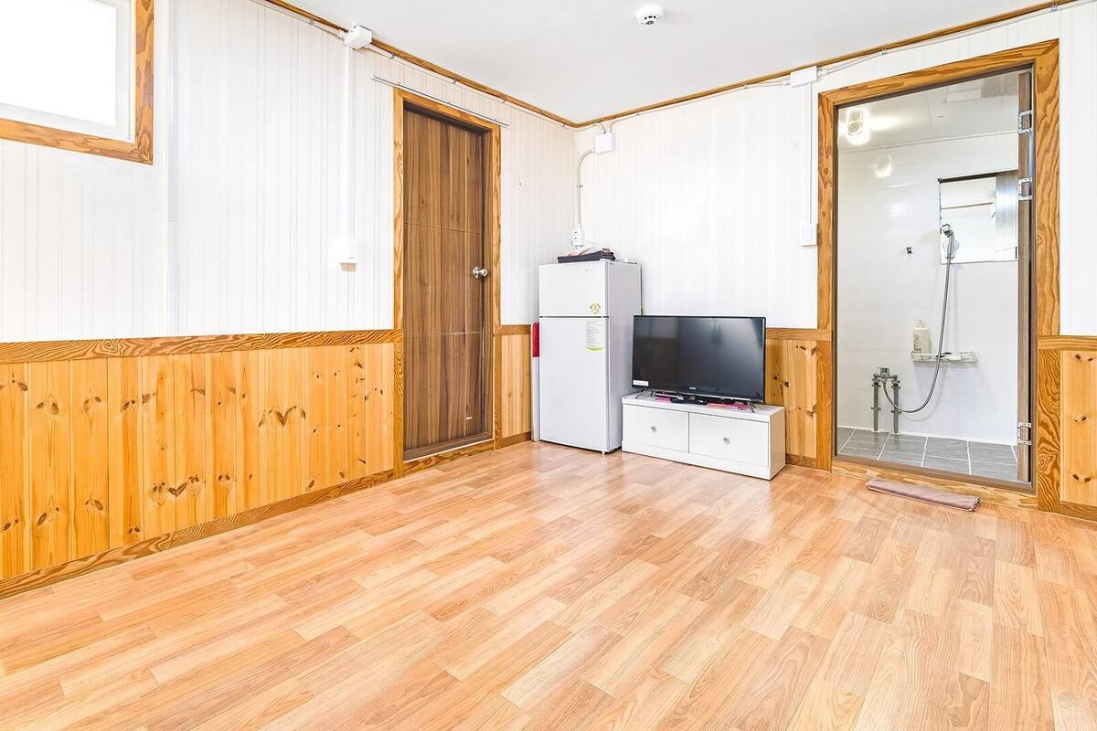 Ein Zimmer mit Holzwänden, einem weißen Kühlschrank, einem Fernseher und einem Duschbereich.