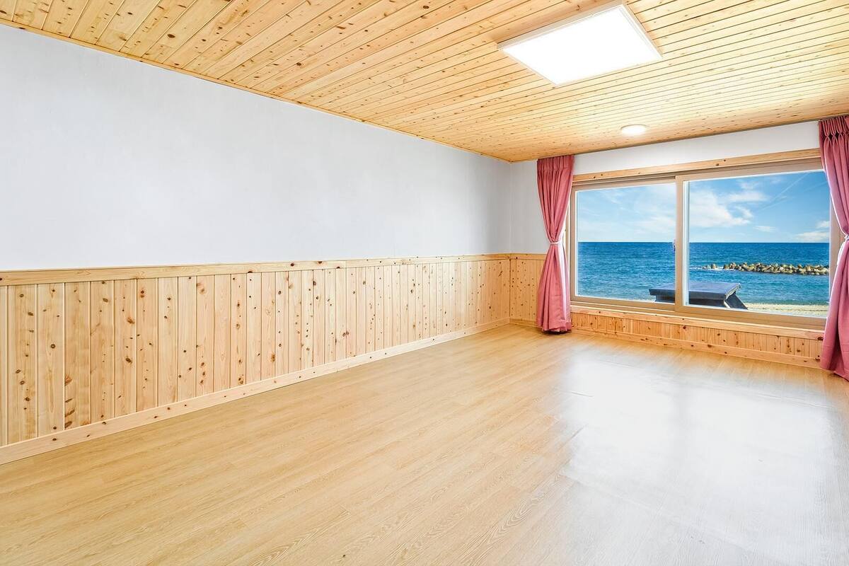 Ein Zimmer mit Holzboden, einem großen Fenster mit Meerblick und einer Holzbalkendecke.