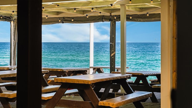 Un espace extérieur aménagé avec des tables et des bancs en bois, offrant une vue sur l’océan.