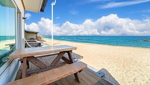 Une vue sur la plage, avec une terrasse en bois et des tables de pique-nique donnant sur l’océan.