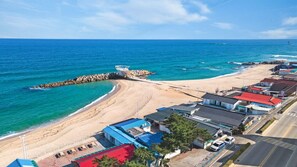Une zone côtière comprenant une plage de sable, une digue rocheuse et une rangée de bâtiments aux toits rouges.
