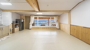 Une chambre avec vue sur l’océan, des murs en bois, un coin cuisine et un plafond avec des poutres apparentes.
