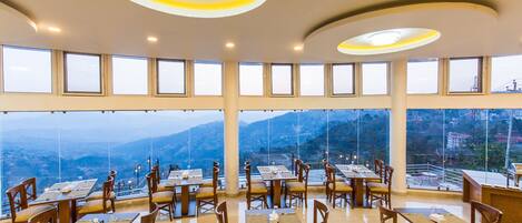A restaurant with multiple tables and chairs, large windows, and a view of the mountains.