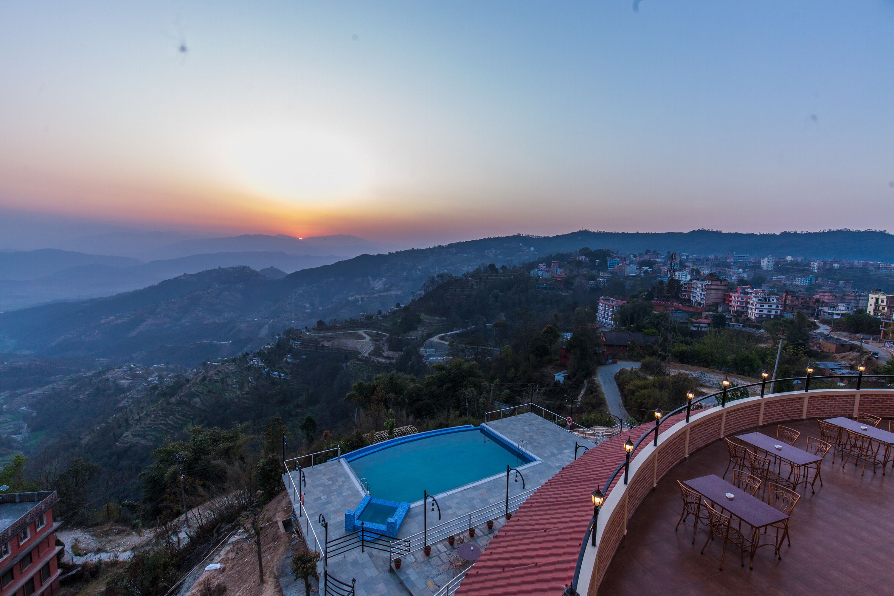 A rooftop pool with a view of a cityscape and mountains during sunset.