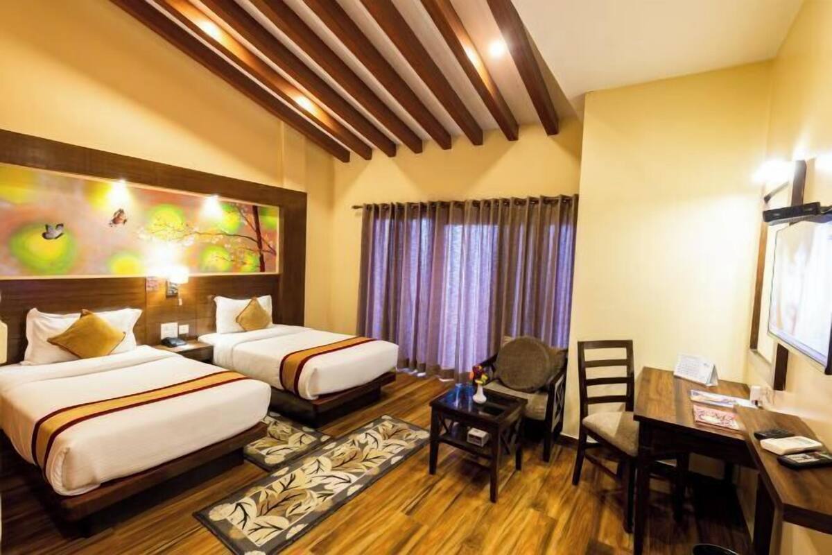 Une chambre d’hôtel avec deux lits, un bureau, une chaise, une petite table et un tableau au mur.