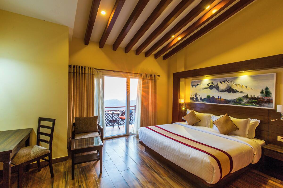 Une chambre d’hôtel avec un grand lit, un bureau et une chaise. Elle dispose d’un balcon avec vue sur les montagnes.