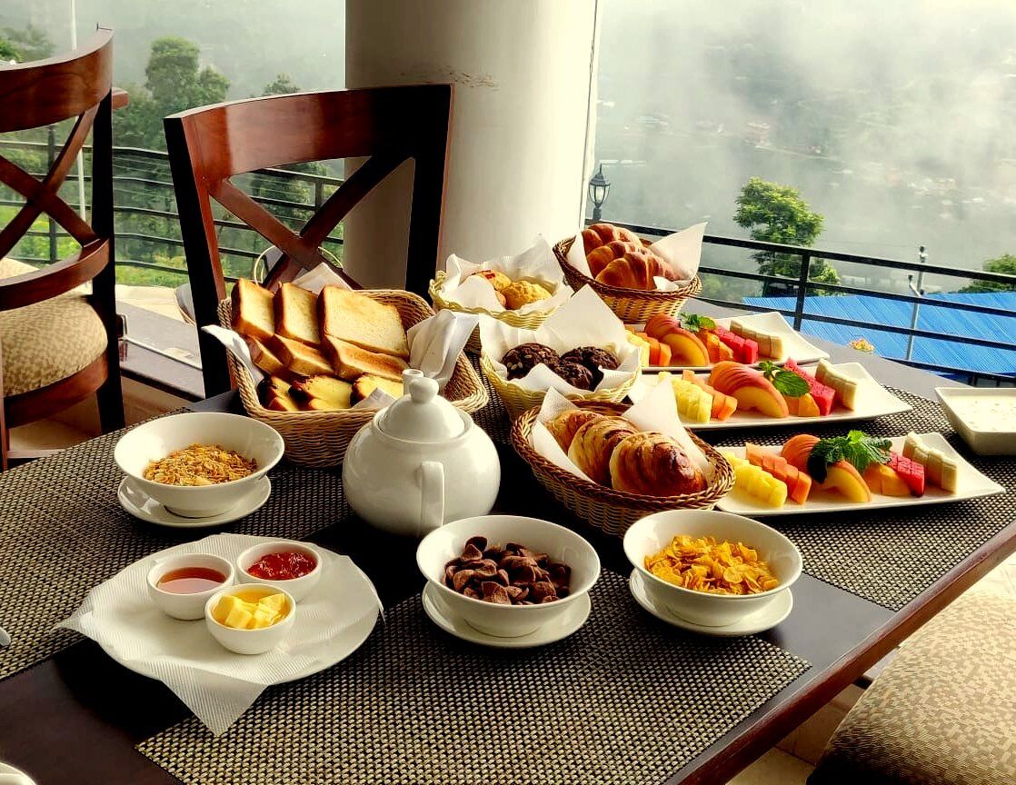 A breakfast buffet with various pastries, fruits, and cereals on a table with a view of a body of water.