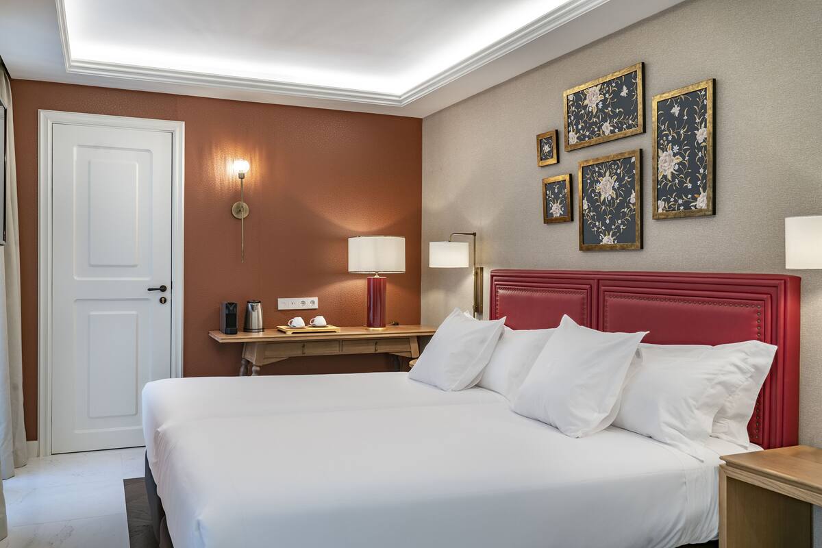 A hotel room with a large bed, a desk with a lamp, and a red headboard.