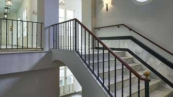 Un interior de varios niveles con una escalera, pisos de mármol y un ventanal circular con vitrales.