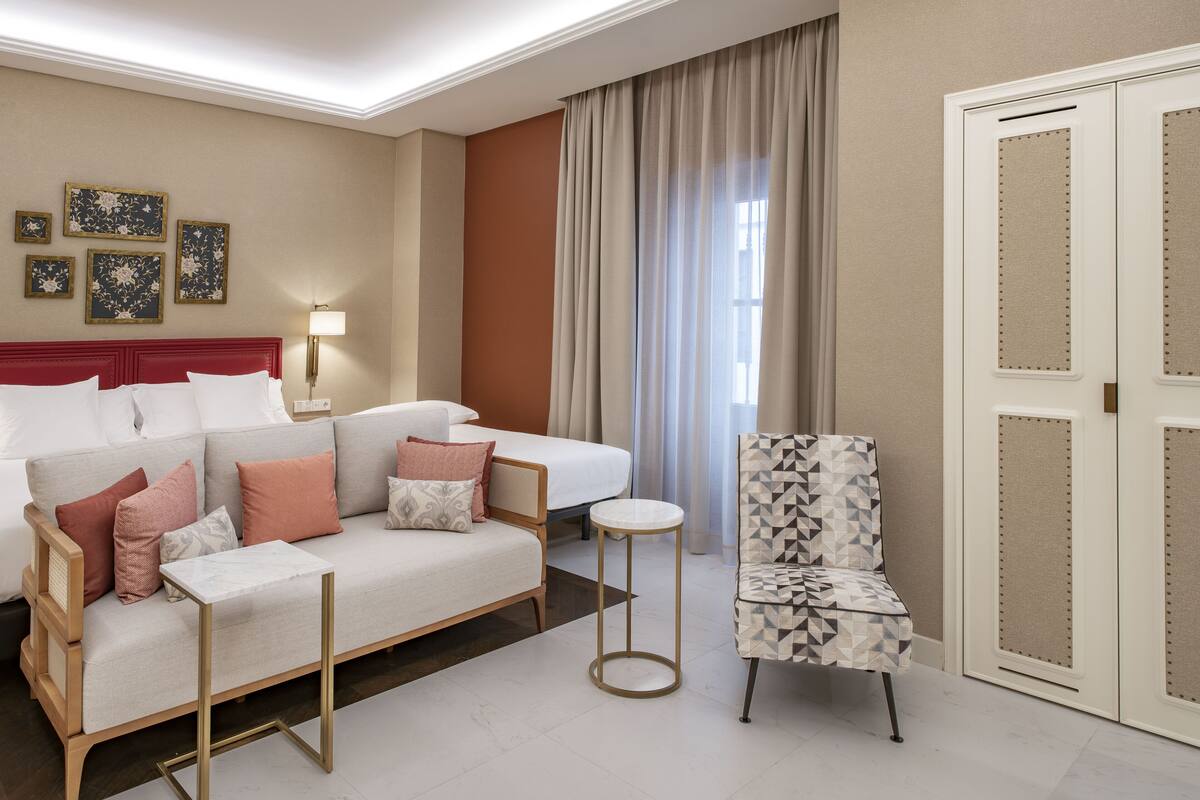 A hotel room with a sofa, a chair, a bed, a bedside table, a lamp, and a wardrobe.