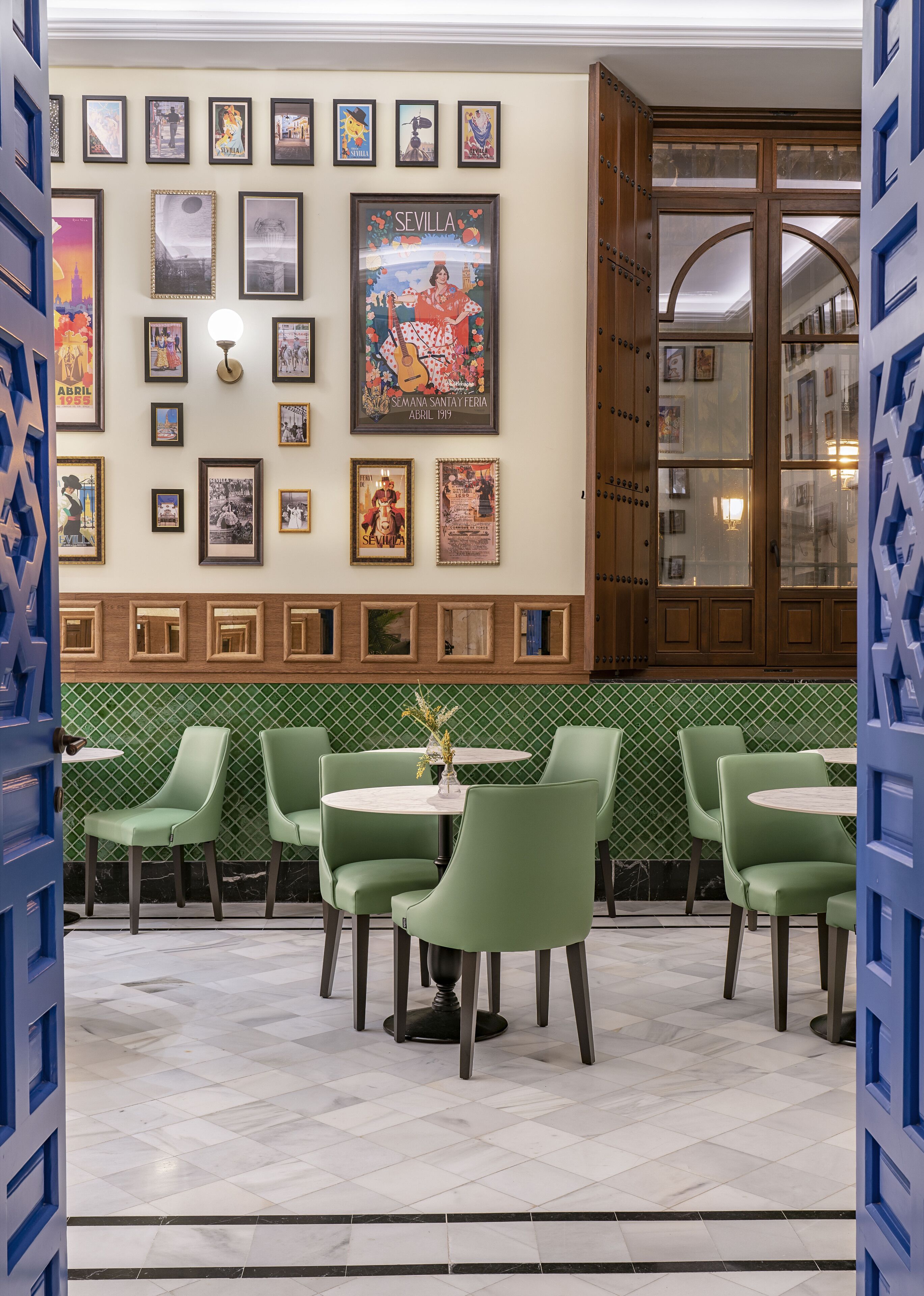 Interior de restaurante con sillas verdes, piso de baldosas y pared decorada con cuadros y carteles.