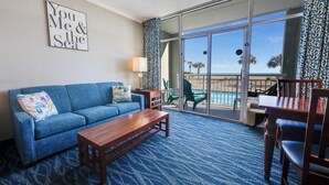 A room with a blue sofa, wooden coffee table, and a view of the sea through large sliding glass doors.