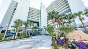A modern hotel with a curved driveway, palm trees, and a brick structure.
