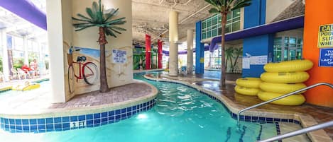 An indoor swimming pool with a no lifeguard on duty sign, a bicycle, and a palm tree mural.