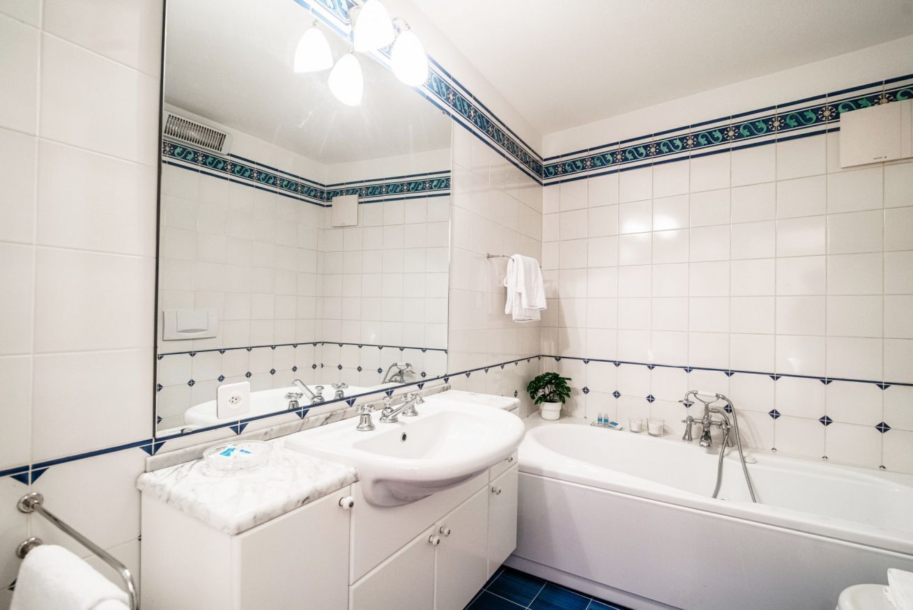 Un bagno con piastrelle bianche, un lavandino, una vasca e uno specchio.