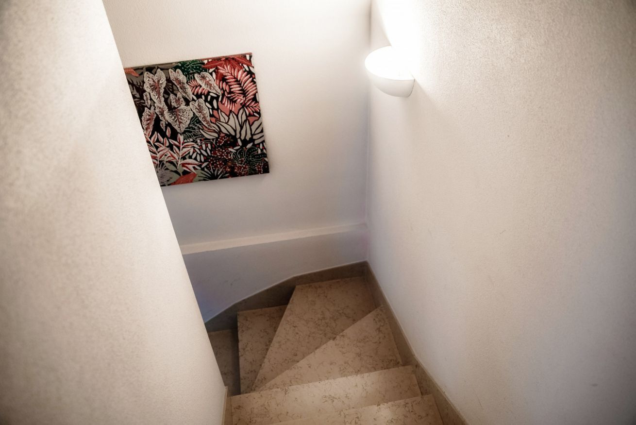Una escalera estrecha con escalones color beige y paredes blancas.