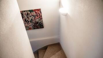 Una escalera estrecha con escalones color beige y paredes blancas.