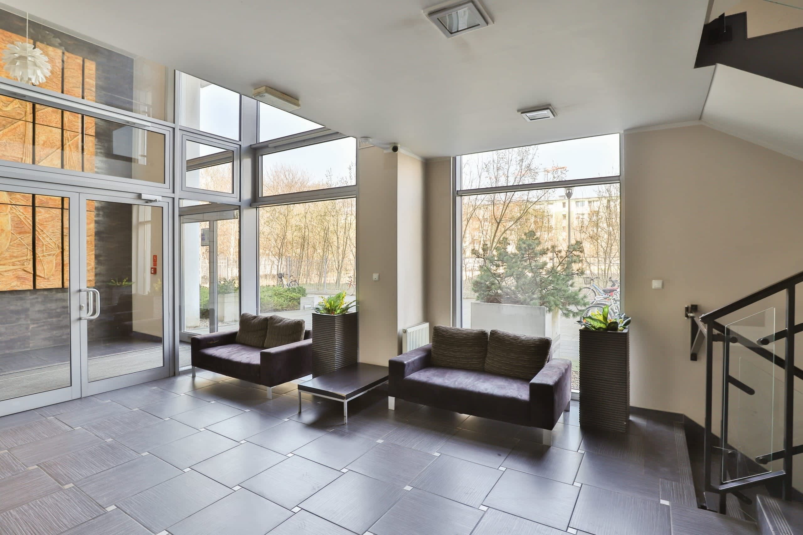 A spacious living area with a modern design, featuring a dark leather sofa, a coffee table, and potted plants.