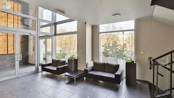 A spacious living area with a modern design, featuring a dark leather sofa, a coffee table, and potted plants.