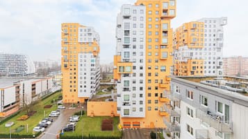 A high-rise residential building with multiple balconies, a parking lot, and a small green area.