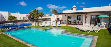A swimming pool with white lounge chairs and a covered patio area.