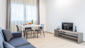 A modern living room with a sofa, a dining table with chairs, a TV on a wooden stand, and a large window with curtains. - Multisuite Palermo (Palermo)