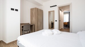 A hotel room with a large bed, a wooden wardrobe, a desk with a chair, a mirror, and a bathroom visible through an open door. - Multisuite Palermo (Palermo)